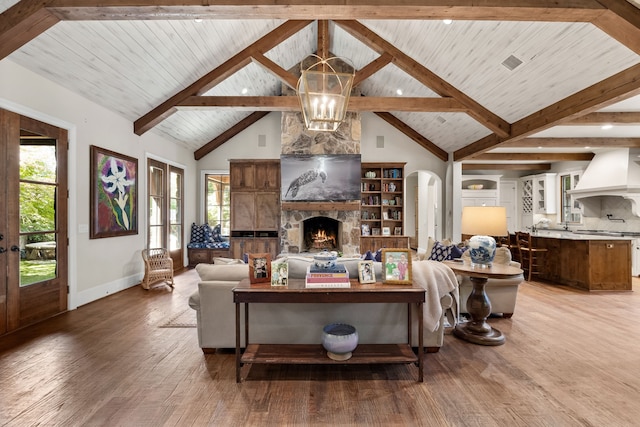 living room featuring baseboards, light wood-style flooring, beamed ceiling, a fireplace, and high vaulted ceiling