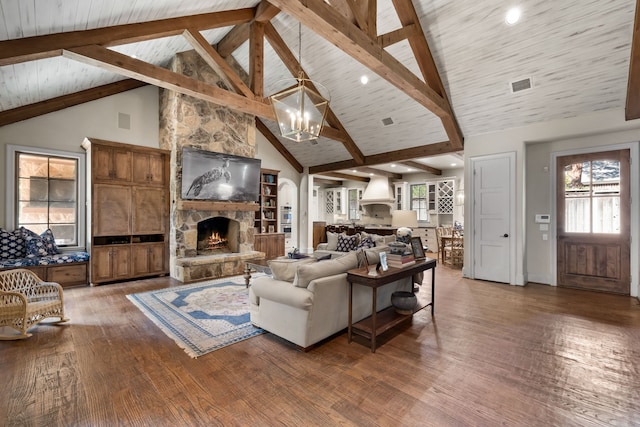 living room with a stone fireplace, beamed ceiling, hardwood / wood-style flooring, and an inviting chandelier