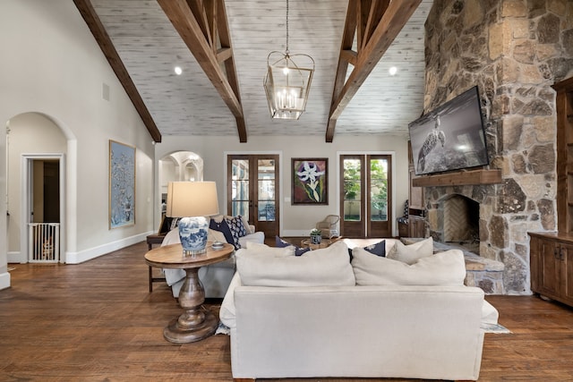 living area with arched walkways, french doors, wood finished floors, a stone fireplace, and beam ceiling