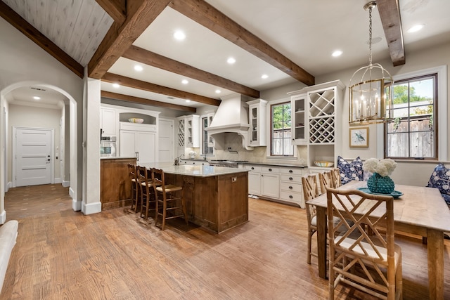 kitchen featuring arched walkways, light wood-style flooring, custom exhaust hood, and a wealth of natural light