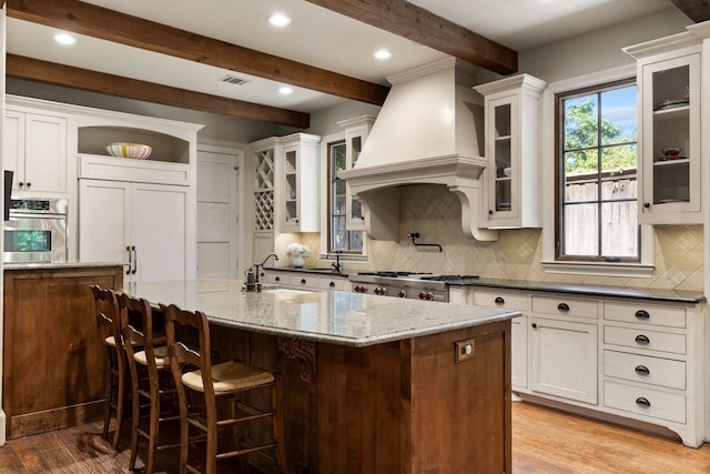 kitchen featuring premium range hood, stainless steel oven, visible vents, beam ceiling, and tasteful backsplash