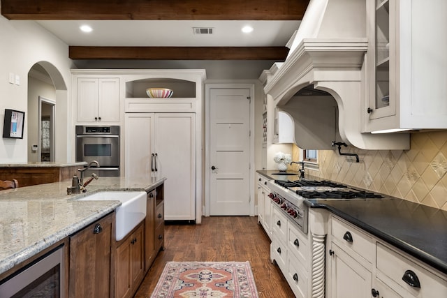 kitchen with stainless steel appliances, dark wood-style flooring, a sink, white cabinets, and beamed ceiling