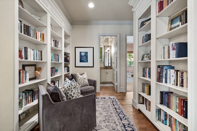 living area with ornamental molding, bookshelves, and wood finished floors