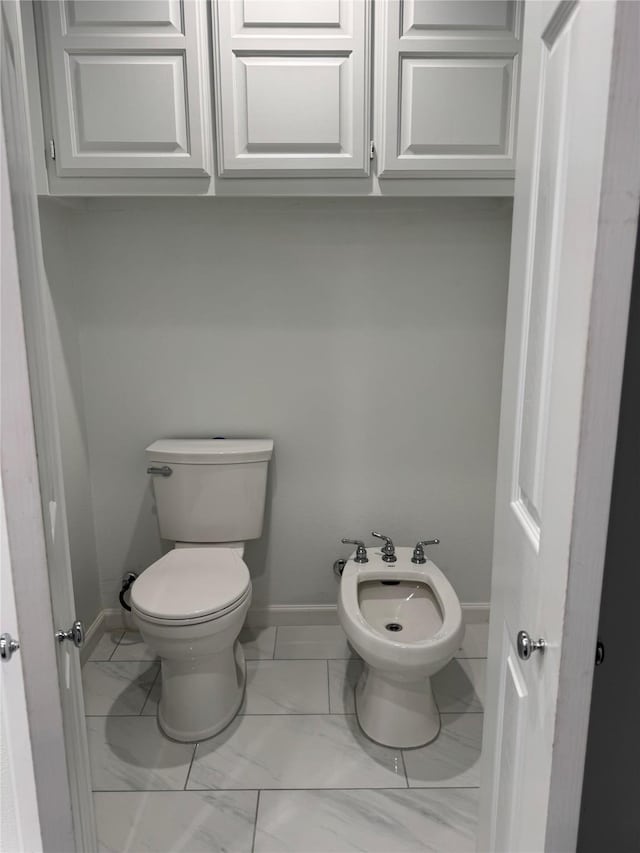 bathroom with marble finish floor, a bidet, toilet, and baseboards