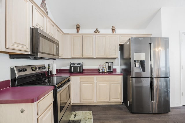 kitchen with stainless steel appliances, dark countertops, dark wood-type flooring, and light brown cabinetry