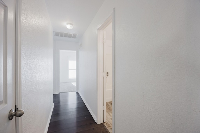 hallway featuring a textured wall, visible vents, dark wood finished floors, and baseboards