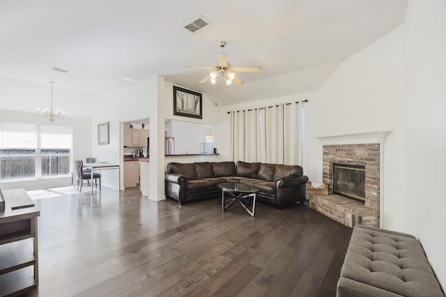 living area with ceiling fan with notable chandelier, dark wood-style flooring, visible vents, vaulted ceiling, and a brick fireplace