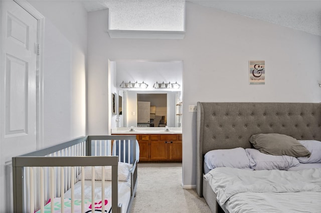 bedroom with lofted ceiling, light colored carpet, a sink, and ensuite bath