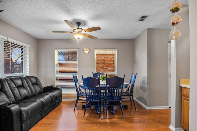 dining area featuring baseboards, visible vents, a ceiling fan, wood finished floors, and a textured ceiling