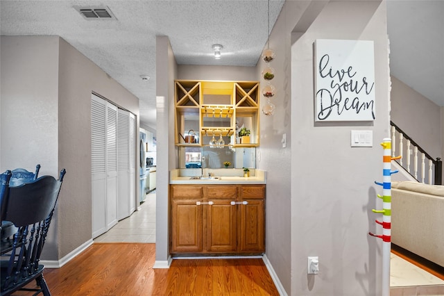 bar featuring visible vents, light wood-style floors, a sink, a textured ceiling, and baseboards