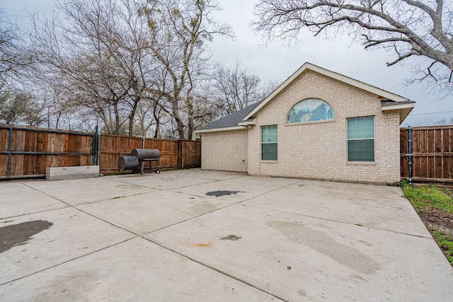 rear view of property featuring brick siding, a patio, and a fenced backyard