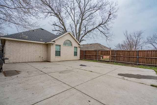 back of house with a patio, brick siding, a shingled roof, and fence