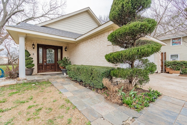 doorway to property with roof with shingles and brick siding