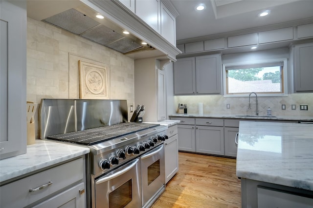 kitchen with light wood-style flooring, gray cabinets, premium range hood, double oven range, and a sink