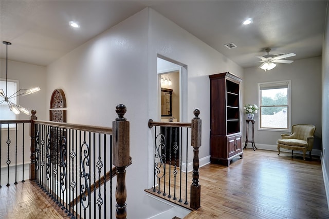 hallway featuring a notable chandelier, visible vents, an upstairs landing, wood finished floors, and baseboards