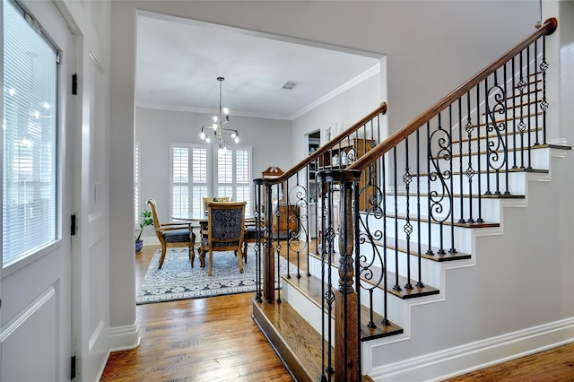 staircase with a chandelier, wood finished floors, visible vents, and crown molding