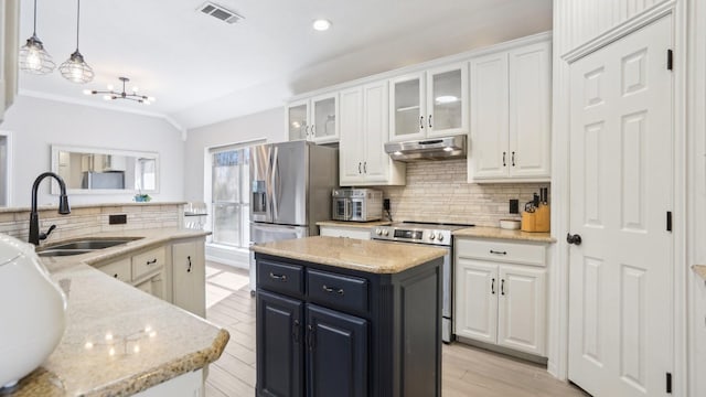 kitchen featuring visible vents, a kitchen island, under cabinet range hood, stainless steel appliances, and a sink