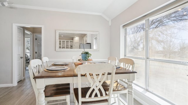 dining space with vaulted ceiling, crown molding, baseboards, and wood finished floors