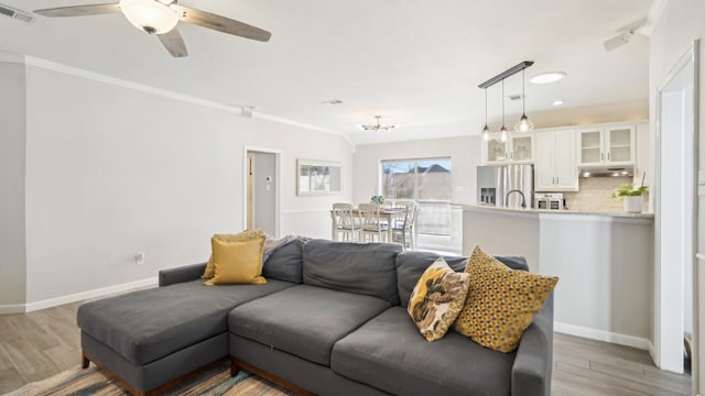 living area featuring visible vents, ceiling fan with notable chandelier, light wood-type flooring, and baseboards