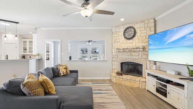 living room with light wood-type flooring, a fireplace, ornamental molding, and a ceiling fan