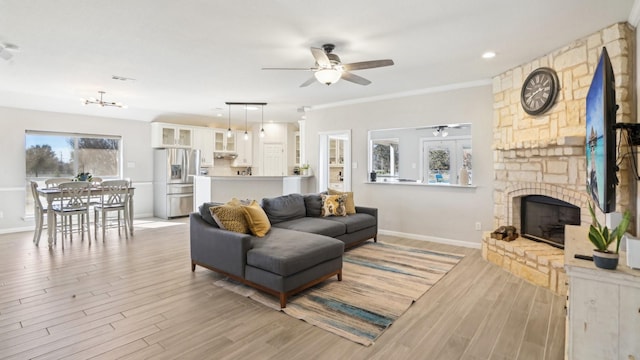 living room with a stone fireplace, baseboards, light wood finished floors, and ceiling fan