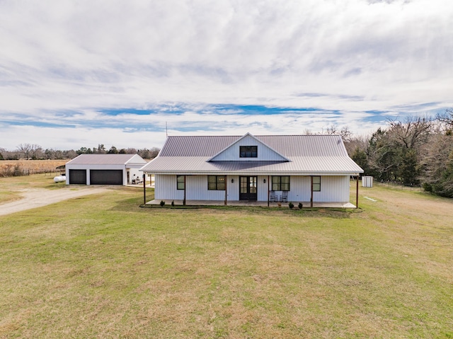 view of front of home with a detached garage, metal roof, an outbuilding, covered porch, and a front yard