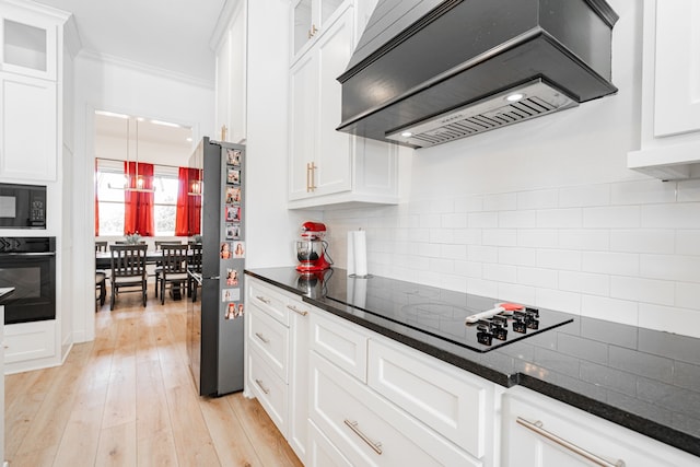 kitchen with light wood-style floors, custom exhaust hood, black appliances, white cabinetry, and backsplash