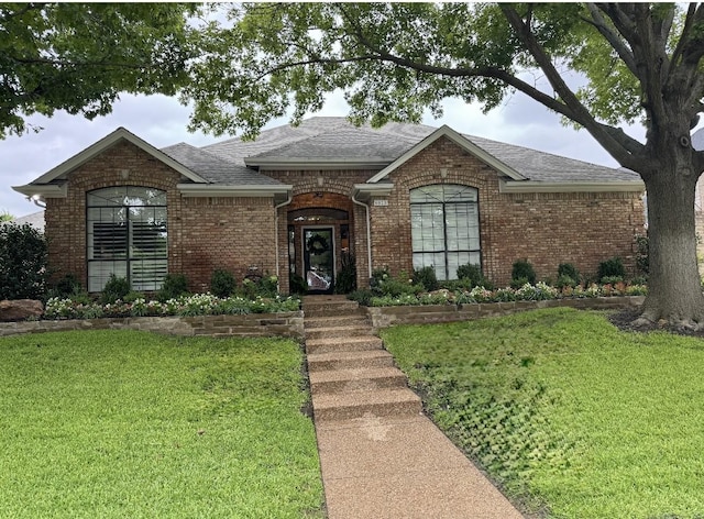 ranch-style house featuring a shingled roof, a front yard, and brick siding