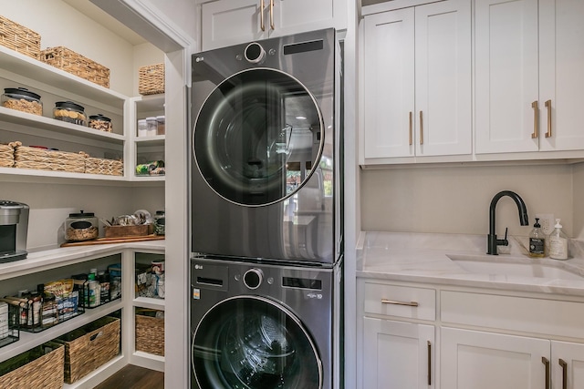 laundry area with stacked washing maching and dryer, cabinet space, and a sink