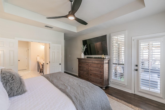 bedroom with wood finished floors, visible vents, baseboards, access to exterior, and a raised ceiling