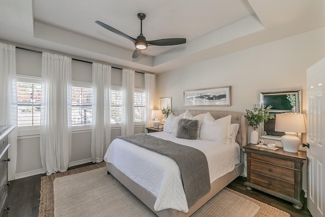 bedroom featuring baseboards, a tray ceiling, and wood finished floors