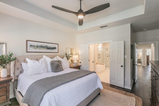 bedroom with visible vents, connected bathroom, dark wood-type flooring, ceiling fan, and a raised ceiling