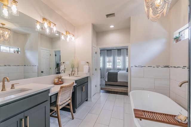 ensuite bathroom with double vanity, a notable chandelier, a soaking tub, and a sink