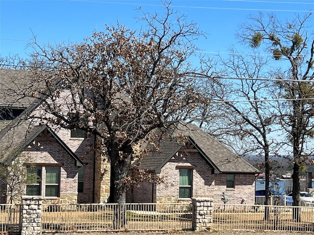 view of front of property featuring roof with shingles, brick siding, and a fenced front yard