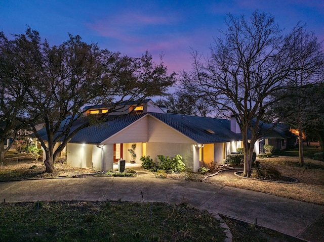 mid-century home with metal roof, curved driveway, and stucco siding