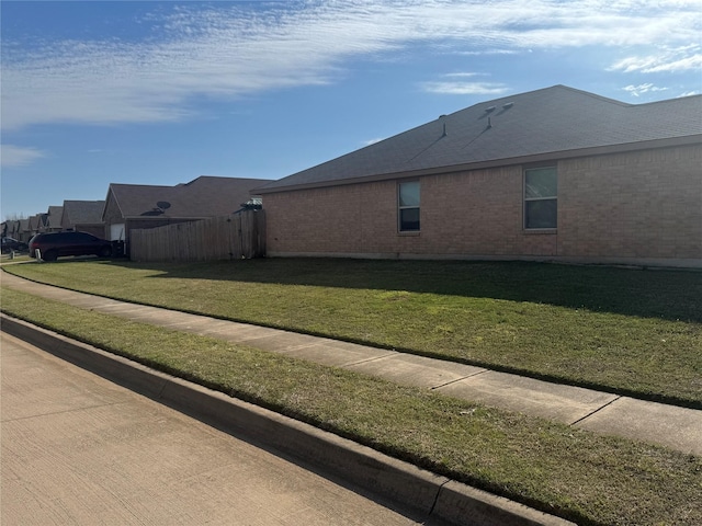 view of side of home with brick siding, a lawn, and fence