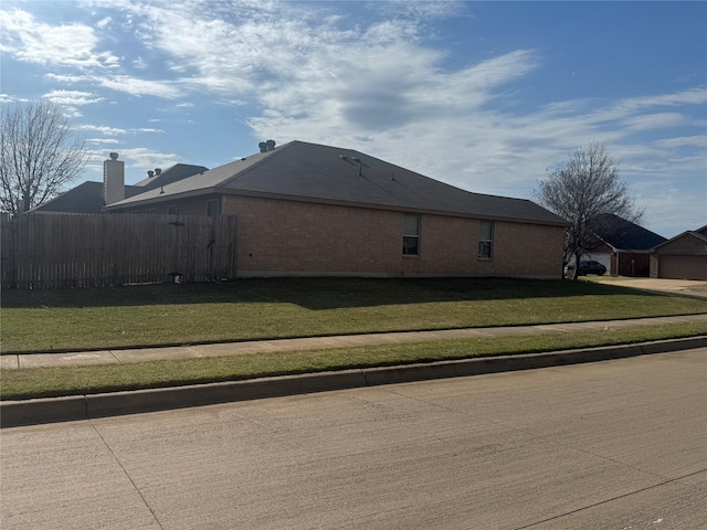 view of side of property with brick siding, a lawn, and fence