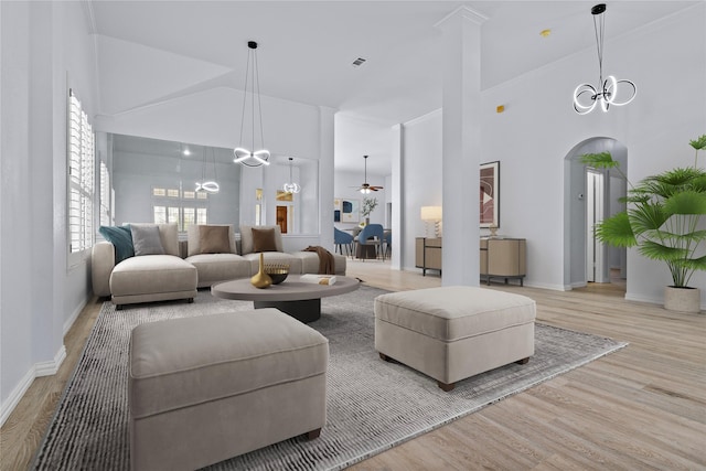 living room with a towering ceiling, arched walkways, wood finished floors, and ceiling fan with notable chandelier