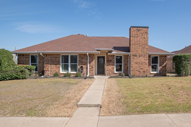 view of front of home with roof with shingles, a chimney, a front lawn, and brick siding