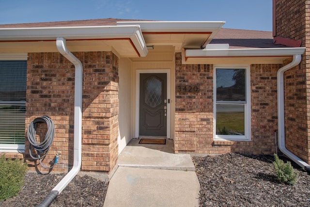 doorway to property featuring brick siding and roof with shingles