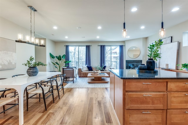 kitchen featuring a glass covered fireplace, light wood-type flooring, dark stone countertops, recessed lighting, and open floor plan
