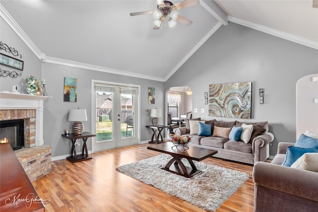 living area with wood finished floors, beamed ceiling, arched walkways, crown molding, and a brick fireplace