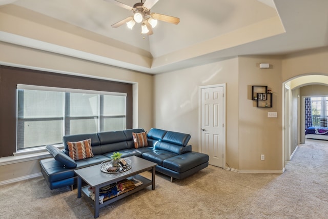 carpeted living room featuring arched walkways, a tray ceiling, a ceiling fan, and baseboards