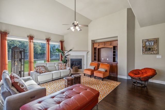 living room with high vaulted ceiling, a tile fireplace, a ceiling fan, baseboards, and dark wood finished floors