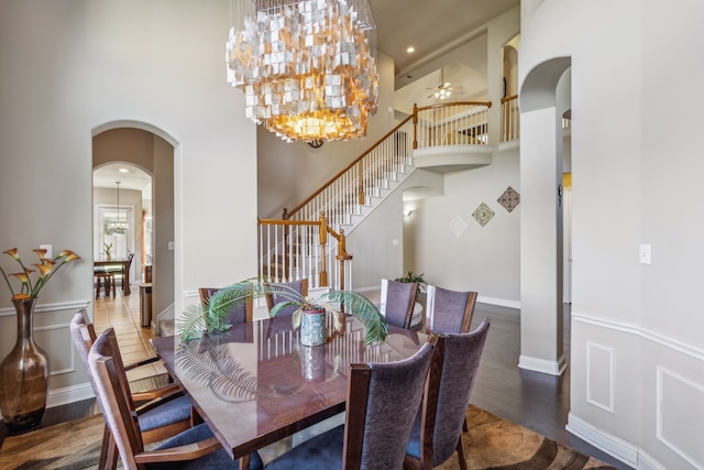 dining space with arched walkways, a high ceiling, stairway, and wood finished floors