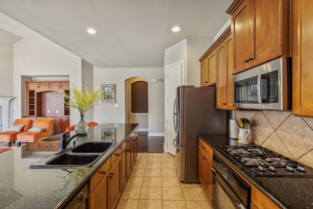 kitchen with arched walkways, a sink, brown cabinets, black appliances, and tasteful backsplash