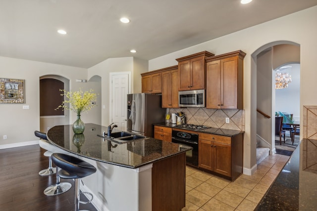 kitchen featuring brown cabinets, stainless steel appliances, decorative backsplash, a sink, and a kitchen breakfast bar