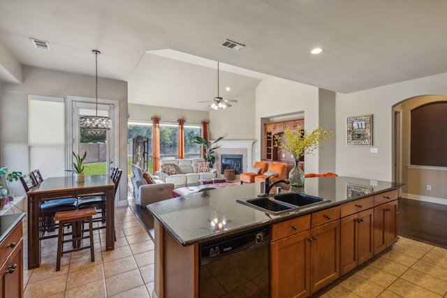 kitchen with black dishwasher, a tiled fireplace, a sink, and visible vents