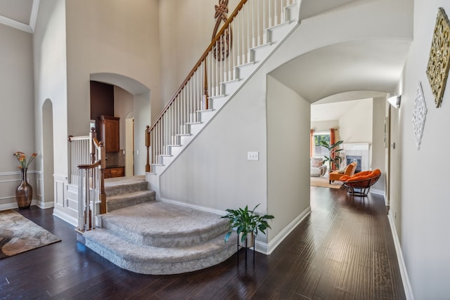 entrance foyer featuring wood-type flooring, a fireplace, a towering ceiling, and baseboards