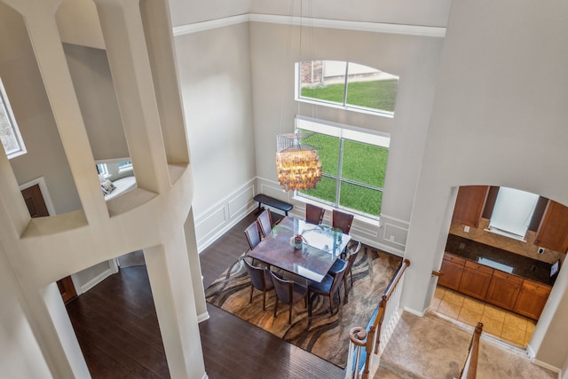 dining room featuring arched walkways, a decorative wall, a towering ceiling, wood finished floors, and a chandelier